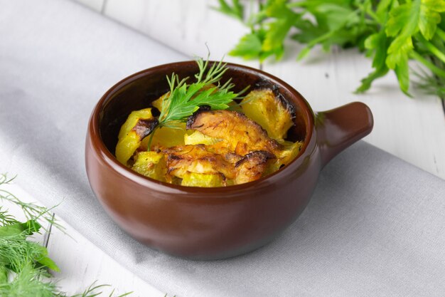 Potatoes, chicken and zucchini baked in a clay pot on a light background.