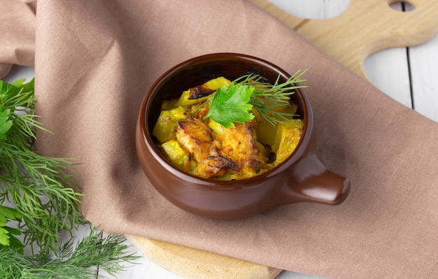 Potatoes, chicken and zucchini baked in a clay pot on a light background.