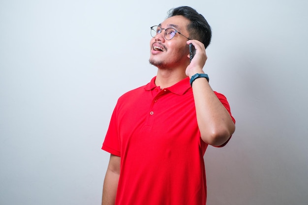 Potrait of young handsome Asian man wearing casual shirt and glasses laughing while making a call