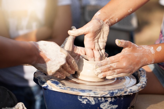 Potter's hands guiding child's hands to help him to work with the pottery wheel