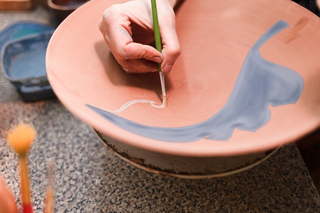 Potter woman paints a ceramic plate closeup