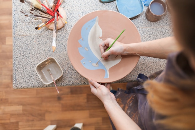 Potter woman paints a ceramic plate.