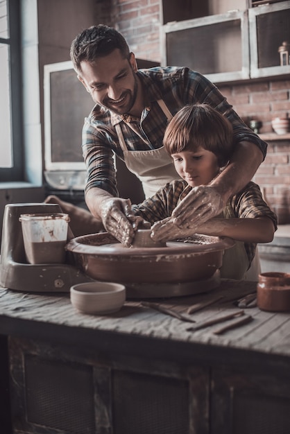 Pottering with father. Cheerful young man and little boy making ceramic pot on the pottery class