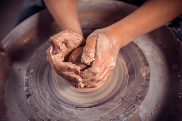 The potters hands are shaped a cup from a clay The process of creating pottery on a potters wheel The master ceramist works in his studio Closeup only hands Crockery from clay own hands