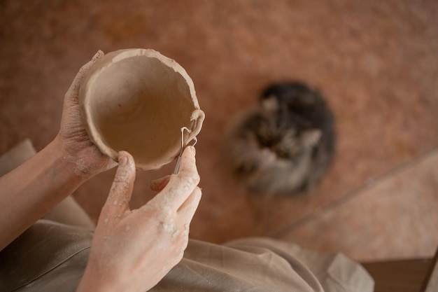 Photo pottery and workshop with clay art concept closeup on the hands of a young woman ceramist with jug of unbaked clay craftsmans working hands hold clay cup and tool