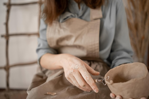 Photo pottery and workshop with clay art concept closeup on the hands of young woman ceramist with jug of unbaked clay craftsmans working hands hold clay cup and tool