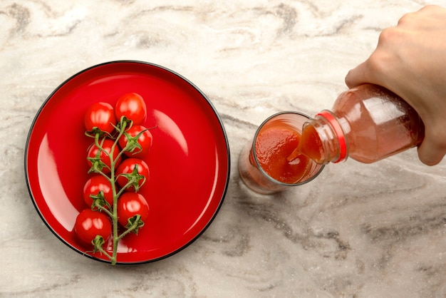 Pour tomato juice into a glass. Hand pours tomato juice from bottle into glass, marble table top background. Banner copy space