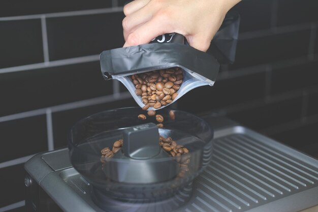 Pouring coffee beans into the espresso machine close up against a black tile wall