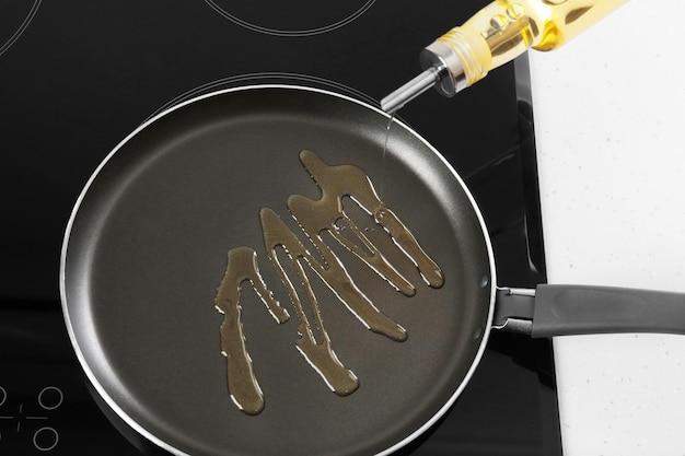 Pouring cooking oil from bottle into frying pan on stove