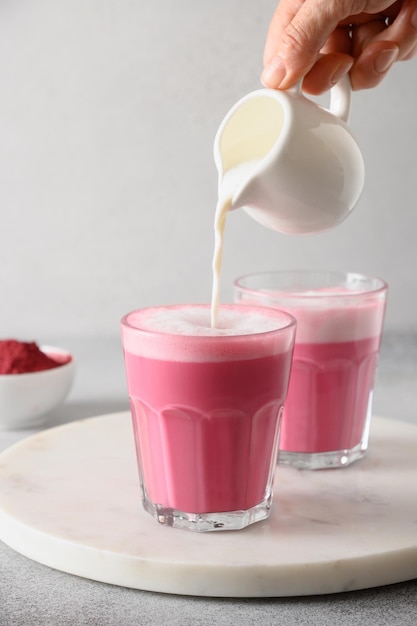 Pouring frothed milk in to beetroot latte in glass on gray background