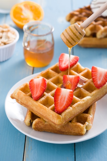 Pouring honey on waffles with strawberry on blue wooden table