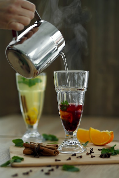 Pouring hot steaming water from steel pot in glass with vitamin drink. winter hot seasonal drinks