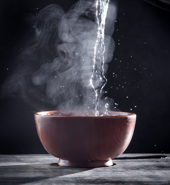 Pouring hot water into into a bowl on a black background