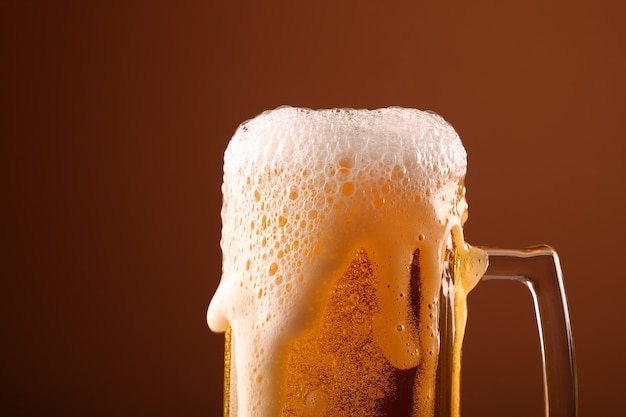 Pouring lager beer in glass mug over brown background