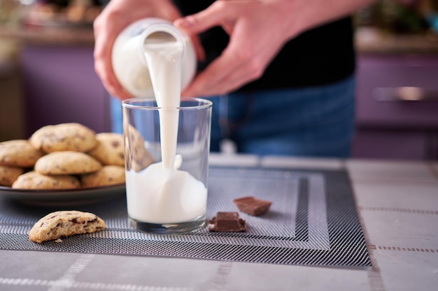 Pouring milk in glass with Homemade chocolate cookies on background