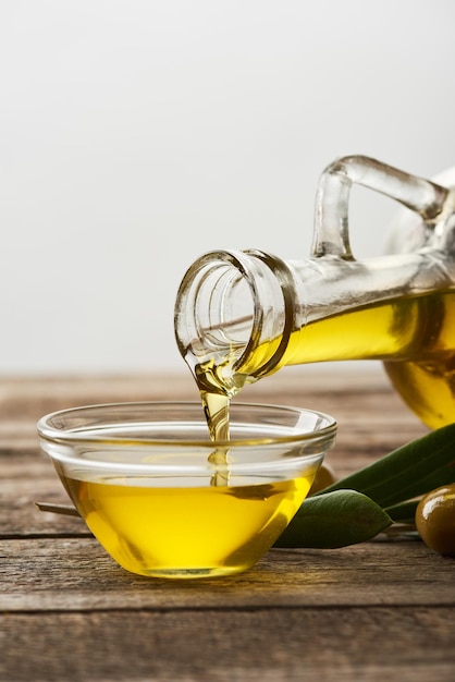 pouring oil into glass bowl olive tree leaves and olives on wooden surface