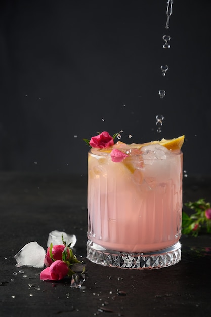 Pouring pink alcoholic cocktail with rose flowers on black background