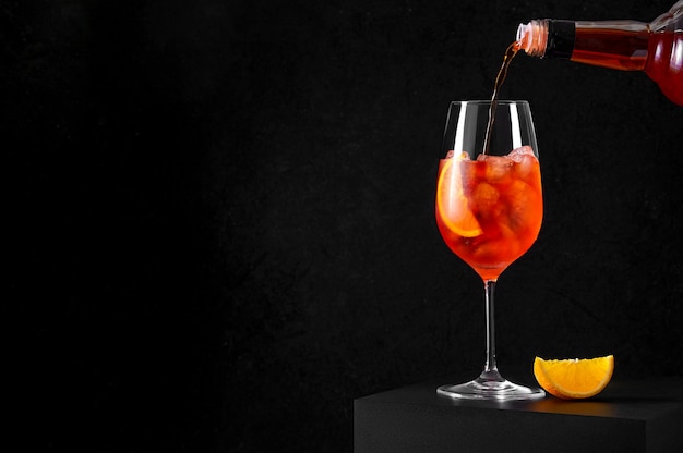 Pouring Spritz Cocktail in wine glass with ice and orange slice on dark background