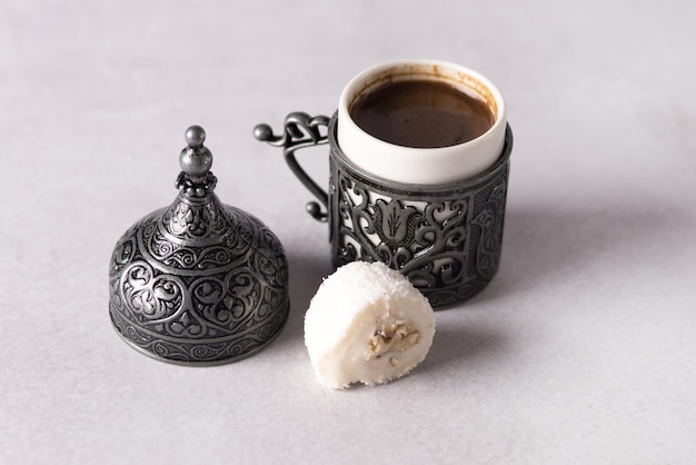 Pouring Turkish Coffee into Traditional Embossed Metal Cup and Coconut Lokum Gray Background