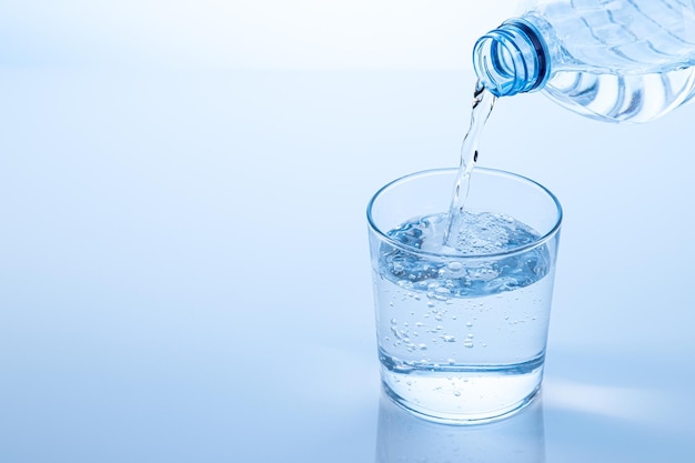 Pouring water from the bottle in to the glass isolated on blue background with copy space