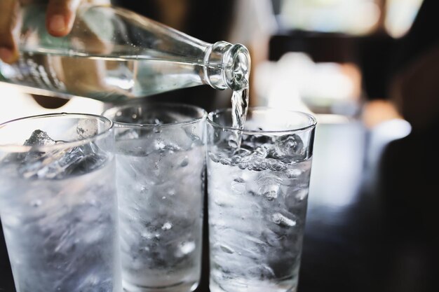 Pouring water from bottle into glass with ice cubes on table