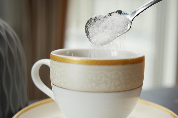 Pouring white sugar in a coffee cup