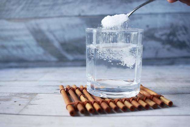 Pouring white sugar in a glass of water on table