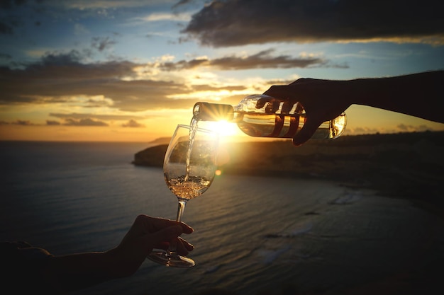 Pouring white wine into the glass against a breathtaking seaside sunset