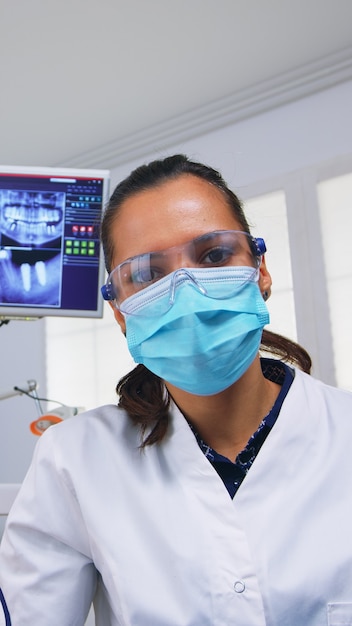 Pov of dentist working on patient mouth hygine in dental office checking teeth problems. Doctor examining in orthodontic office with light lamp and sterilized utensils, close-up face in medical mask.