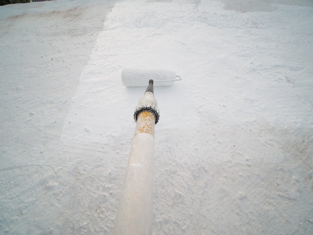 POV shot. Waterproofing roof with roller and white silicon paint.