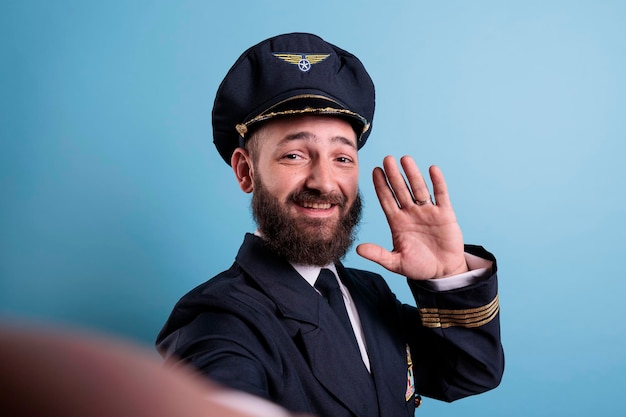 Pov of smiling aviator greeting at camera, taking selfie on front smartphone camera, fpv. Middle aged airplane pilot in aviation uniform, making photo on mobile phone. First person view