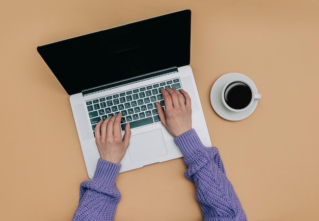 POV view on female hands over laptop computer next to cup of coffee on brown background