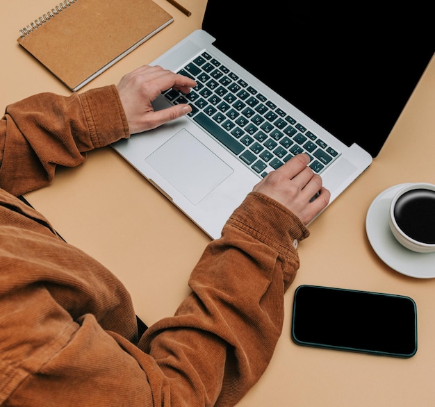 POV view on female hands over laptop computer next to cup of coffee and mobile phone on brown background