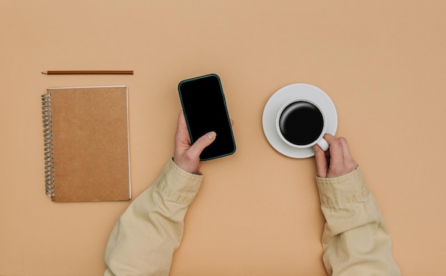 Pov view on female hands with smartphone next to notebook and cup of coffee on brown background