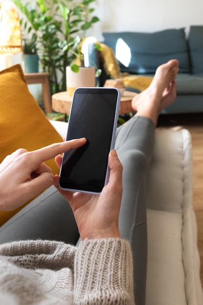 POV of young caucasian woman using mobile phone relaxing at home in cozy living room apartment Vertical image Social media concept