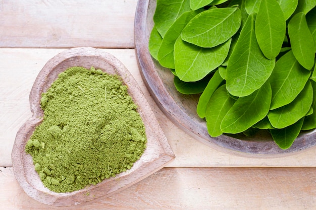 Powder and moringa leaves in bowl on wooden background