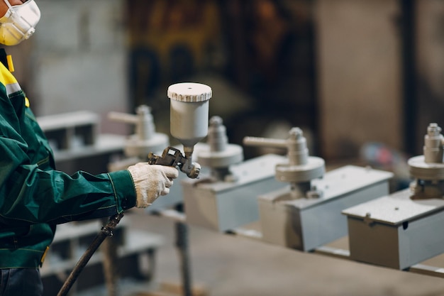 Powder primer coating of metal parts Worker man in a protective suit sprays powder paint from gun on metal product construction at factory plant