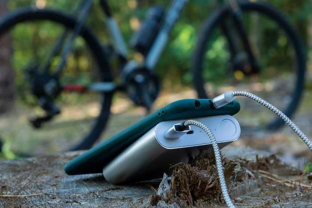 Power bank charges a smartphone in the forest on the background of a bicycle.