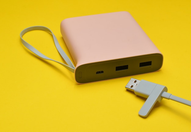 Power bank for charging smartphones and gadgets with a usb cable close-up on a yellow background. Modern technologies.