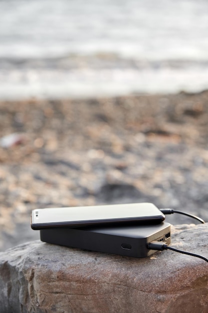 Powerbank charges the phone on the beach by the sea