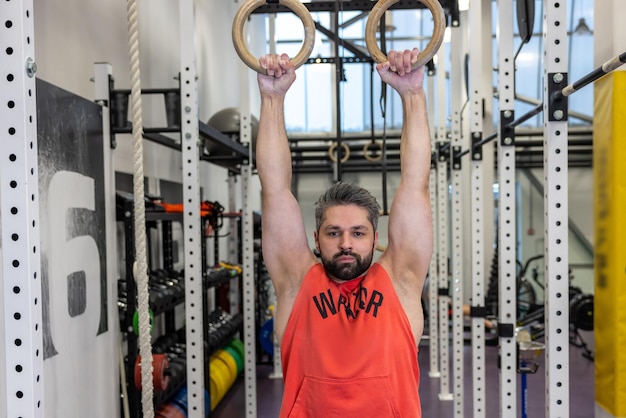 Powerful bearded man exercising with gymnastic rings at gym