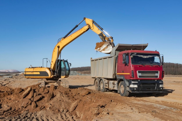 A powerful crawler excavator loads the earth into a dump truck against the blue sky Development and removal of soil from the construction site