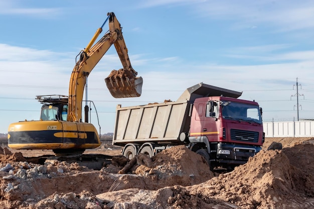 A powerful crawler excavator loads the earth into a dump truck against the blue sky Development and removal of soil from the construction site