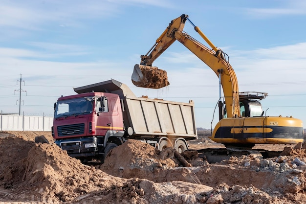 A powerful crawler excavator loads the earth into a dump truck against the blue sky Development and removal of soil from the construction site