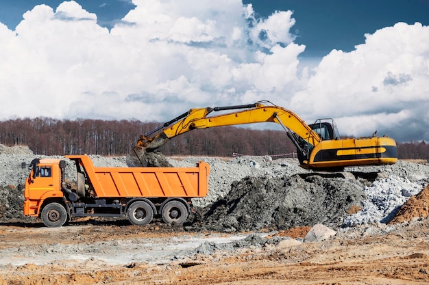 A powerful crawler excavator loads the earth into a dump truck against the blue sky Development and removal of soil from the construction site