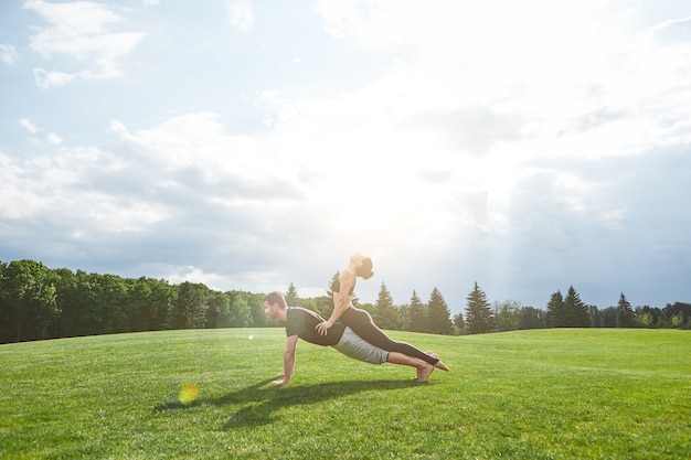 Practicing acro yoga together strong man is staying in plank on a grass in nature