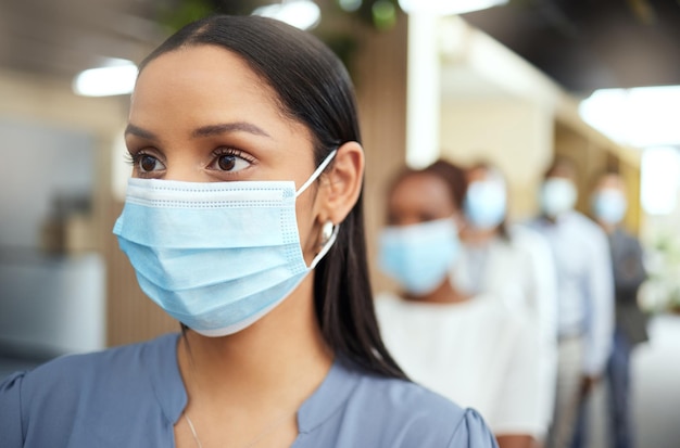 Practicing caution Cropped shot of an attractive young businesswoman wearing a mask while standing at the head of a queue in her office