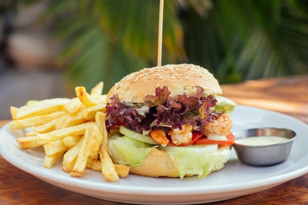 Prawns burger and french fry on table tropical sea palms tree and beach background