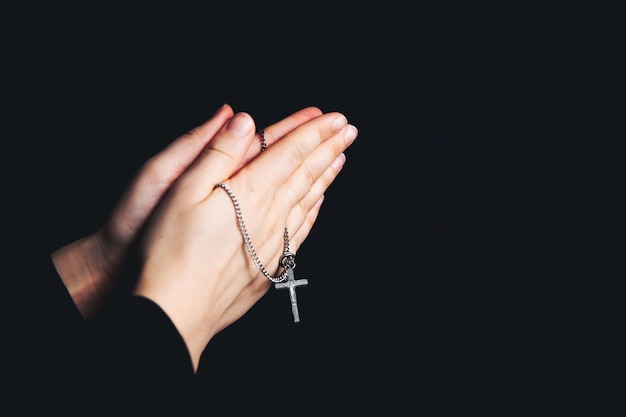 Praying hands holding a rosary Closeup holding necklace with crosspray for god in the dark religious Christian symbol