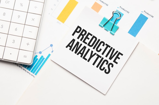 PREDICTIVE ANALYTICS text concept. Office workplace table with calculator, graphs, reports and the text Budget 2021 on a small piece of paper on multicolored background.